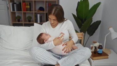 Yatak odasında bebek beşiği yapan, sevgi ve özen gösteren, arka planda bitki ve kitap raflarıyla aile bağlarını gözler önüne seren bir kadın..