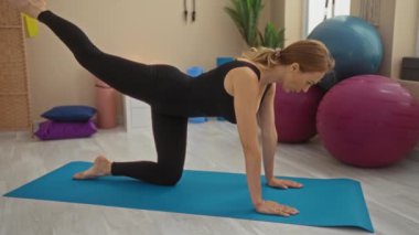 Spor salonunda yoga minderinde egzersiz yapan bir kadın spor salonunun içinde spor yaparken spor yaparken siyah kıyafetler ve spor yaparken spor topları giyiyor..