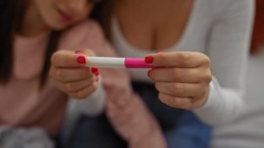 Hamilelik testi tutan bir kadın. Bu arada genç kız evde oturup izliyor. Aile bağlarını ve içerideki neşe dolu beklentileri simgeliyor..