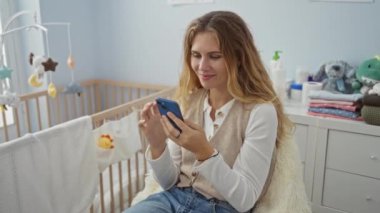 Kadın gülümserken rahat yatak odasında beşik, rahat iç mekan atmosferi ve modern yaşam tarzıyla akıllı telefon kullanıyor..