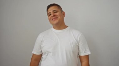 Beyaz gömlekli gülümseyen genç İspanyol adam kolları bağlı beyaz arka plan duvarının üzerinde duruyor.