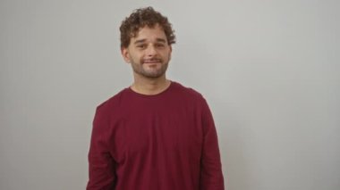 Genç İspanyol adam ayakta, tişörtünü giymiş, elleri ile kaplanmış, şaşırmış ve izole edilmiş beyaz bir arka planda gülümsüyor.