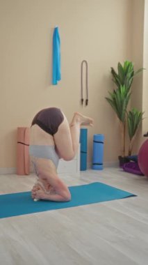 Spor salonunda yoga yapan bir kadın, mavi paspas bitkileri ve iç dekorasyonunu gösteren minimal dekorla sakinleştirici bir ortamda kadın fitness için aktif yaşam tarzını gösteriyor.