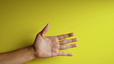 Parlak sarı bir arka plana yayılmış parmakları olan bir adamın yakın çekimi.