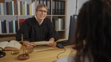 Kadın yargıç, mahkeme salonunda bir kadın müvekkil ile dava belgelerini tartışıyor. Mahkeme salonunda yasal kitaplar ve adalet terazileri görülüyor..