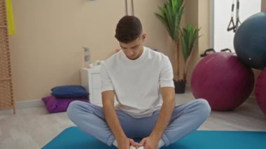 Spor salonundaki yoga minderinde, spor aletleriyle bacak bacak bacak üstüne atmış genç bir adam içeride sakin meditasyon pratiği yapıyor..