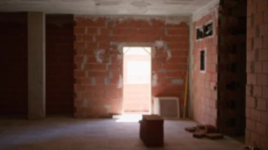 Tamamlanmamış bir inşaat alanının iç görünümü tuğla duvarlar, çözülmüş arka plan, ve açık bir kapıdan süzülen seyrek ışık.