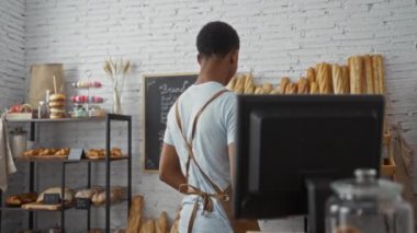 Pastanede çalışan bir adam, dükkânın içinde ekmek rafları ve ekmek bulunan ekmek vitrininin önünde kadına kahve veriyor.