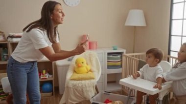 Sıcak yatak odasında oyuncaklarla ve beşiğiyle iki çocuğun fotoğrafını çeken gülümseyen bir kadın, evde sevgi dolu bir aile anını yakalıyor..