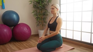 Sakin bir spor salonunda yoga yapan bir kadın. Egzersiz topları ve pencereden süzülen güneş ışığı ile sakin meditasyonu ve odaklanmayı somutlaştırıyor..