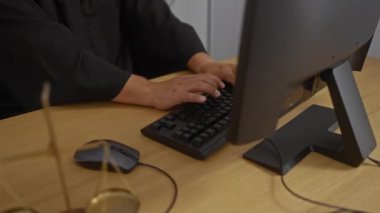 Yargıç, arka planda yasal materyallerin bulunduğu bir ofiste bilgisayar üzerinde çalışıyor.