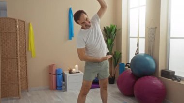 Olgun bir adam spor salonunda spor topları, yoga minderleri ve esneme bantlarıyla egzersiz yapıyor, sağlıklı bir yaşam tarzını kucaklıyor ve spa benzeri bir yerde rahatlıyor..