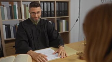 Siyah cüppeli yargıç, arka planda kitap ve dosyalarla mahkeme salonunda bir kadına yasal danışma ortamı sunuyor.