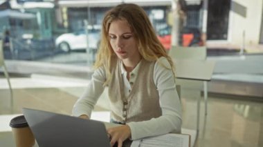 Ofiste dizüstü bilgisayarda çalışan kadın sarışın bir yetişkinin gazete ve kahveyle yoğun bir şekilde ışığa odaklandığını gösteriyor..