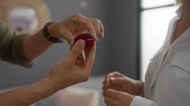 Erkekler, oturma odasında yüzükle kadınlara evlenme teklif eder. Özel bir anda ellerini yakın plan çekerler..