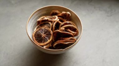 Bir kase kurutulmuş portakal diliminin, gri bir yüzeye yakın plan, kırsal bir aperatif veya yemek malzemesi konsepti için, turunçgil, susuz ve sağlıklı besin elementleri vurgulanıyor.