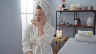 Spa merkezinde dinlenen beyaz bornoz giymiş bir kadın. Huzurlu bir sağlık odasında mumlar ve çiçeklerle esniyor ve esniyor.