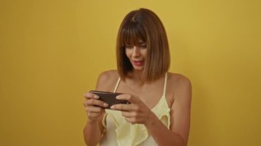 Sarı bir bluz giyerken izole edilmiş sarı bir arka plana karşı akıllı telefona odaklanan genç bir kadın.
