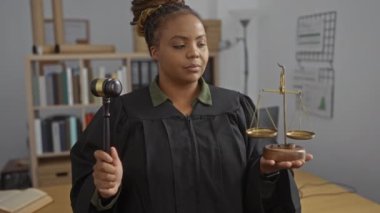 Elinde tokmak ve teraziler tutan kadın, mahkeme salonunda profesyonel bir Afro-Amerikan yargıcı tasvir eden kitap ve yasal belgelerle dolu bir ofiste adaleti simgeliyor.