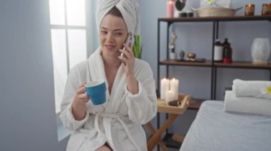 Kaplıcada, arka planda mumlar olan mavi bir bardakla konuşan bir kadın, sağlık deneyiminden zevk alıyor.