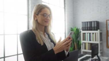 Modern ofis ortamında akıllı telefon kullanan, parlak doğal ışık ve şık dekorlarla çevrili bir kadın, çağdaş bir çalışma ortamında profesyonel bir ilişki gösteriyor..