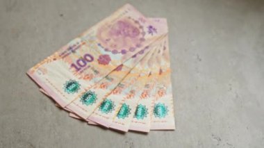 Arjantin para birimi, özellikle 100 peso banknotlar, canlı tasarım ve güvenlik özellikleri sergilenen beton yüzey sergilenen bir pervaneye yerleştirilmiş..