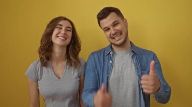 Erkek ve kadın gülümsüyor ve parlak sarı bir arkaplan karşısında başparmak işareti yapıyor, ilişkilerinde mutluluk ve pozitiflik sergiliyorlar.