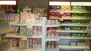 Bulanık arka plan ve çeşitli renkli paketlenmiş ürünlerle dolu raflarla odaklanmış süpermarket koridoru ve odak dışı ögeler bir bokeh etkisi yaratıyor