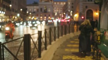 Roma 'nın eski şehir sokağında yürüyen kadın ve adamla bulanık bir gece sahnesi, sokak lambaları ve arabalarla bokeh etkisi altında.