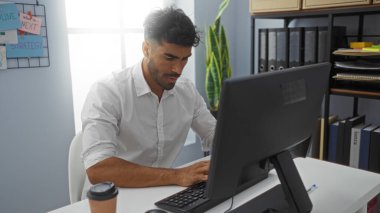 Modern ofiste bilgisayar ve kahveyle çalışan genç bir İspanyol.