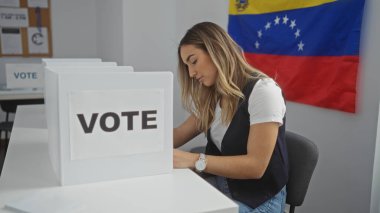 Seçim odasında arka planda Venezuela bayrağı olan genç, sarışın bir kadın oy veriyor ve demokratik sürece olan bağlılığını vurguluyor..