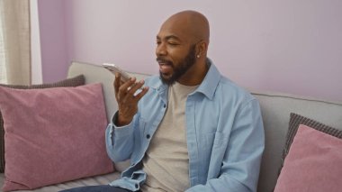 Genç adam oturma odasında bir kanepede otururken akıllı telefondan konuşuyor.