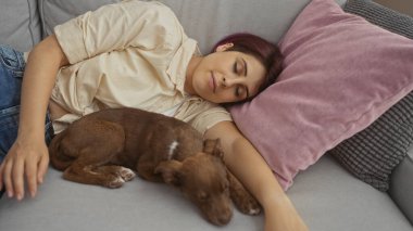 Evinin oturma odasındaki kanepede köpeğiyle uyuyan genç bir kadın.