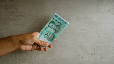 Çince Yuan 'ı elle tutarak beton bir arka plana karşı koymak