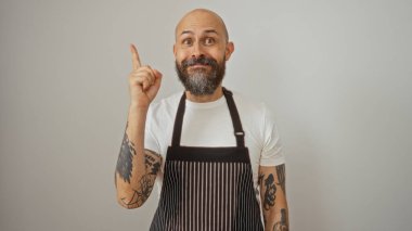 Sakallı, önlüklü, yukarı doğru bakan, beyaz bir arka planda izole edilmiş, dövmeli bir kol ve bir portrede neşeli bir ifade sergileyen İspanyol bir adam..