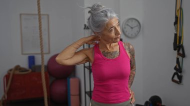 Spor salonunda boynunu içeri doğru uzatan yaşlı bir kadın.