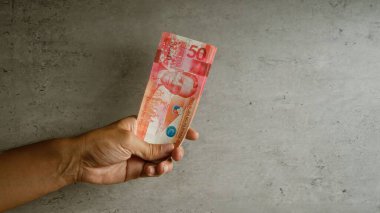 Elinizde somut bir arkaplana karşı Filipinli bir peso banknotu var. Para biriminin detaylarını ve insanların parmaklarını vurguluyorsunuz..