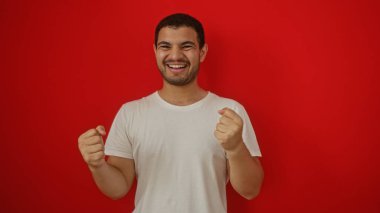 Yakışıklı, genç, İspanyol bir adam gülümseyen ve kırmızı arka plan duvarına yumruk sallayan..