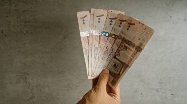 Birkaç Suudi Arabistan riyal banknotunu beton bir arka planda tutarken