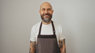 Sakallı, dövmeli, önlük takan, izole edilmiş beyaz bir arka plana sırıtan yakışıklı İspanyol bir adam.