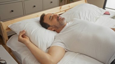 Orta yaşlı bir adam rahat bir yatak odasında rahat bir şekilde uzanıyor.