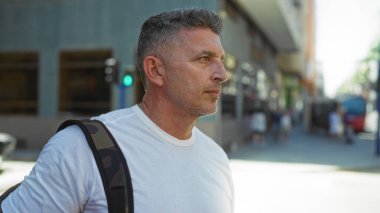 Gündüz vakti şehir sokaklarında yürüyen, ciddi bir ifadeye sahip yakışıklı orta yaşlı bir adam..