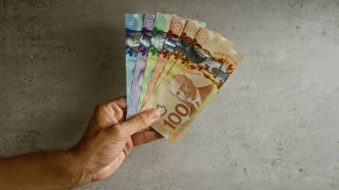 Elele tutuşan Kanada doları banknotları somut arka planda renkli para birimini ve finansal konsepti gösteriyor