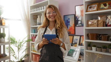 Kadın elinde tabletle bir dükkânda çalışıyor ve gülümsüyor. Etrafı tuhaf dekoratif eşyalarla çevrili..