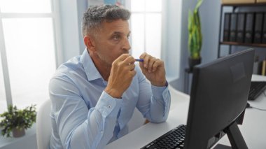 Ofis masasında çalışan orta yaşlı bir adam yoğun bir şekilde bilgisayar ekranına odaklanıyor.