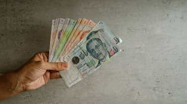 Adam beton bir arka planda yelpazelenmiş Singapur doları tutuyor.