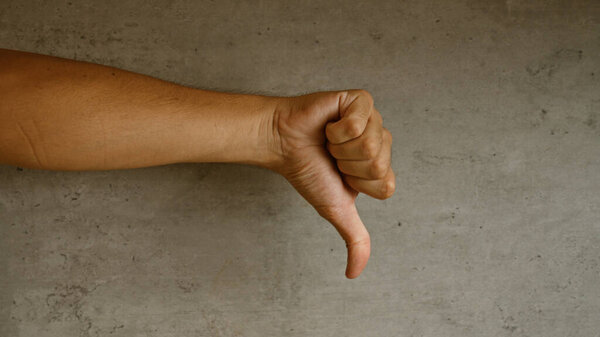 Рука делает жесты вниз на бетонном фоне, подразумевая неодобрение или неприязнь.