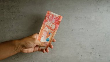 50 peso 'luk Filipin banknotunu, desenli beton bir arka plana karşı elinde tutan adam, elinde banknotun tasarımı ve canlı renklerinin canlı detaylarıyla sergiliyor..