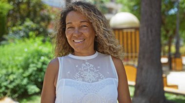 Güler yüzlü kadın yemyeşil bir şehir parkında güneşli bir günün tadını çıkarıyor..