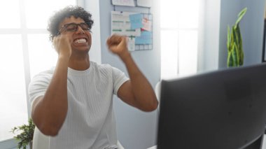 Genç adam işyerindeki başarısını kutluyor. Parlak ve modern ofis ortamında heyecan ve başarı sergiliyor..